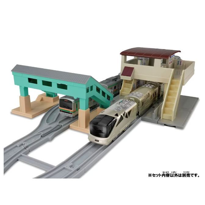 A toy train set with two trains, a station, and a pedestrian bridge.