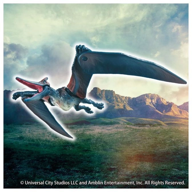  Pteranodon toy with long beak and wings, flying over a grassy landscape with mountains in the background.