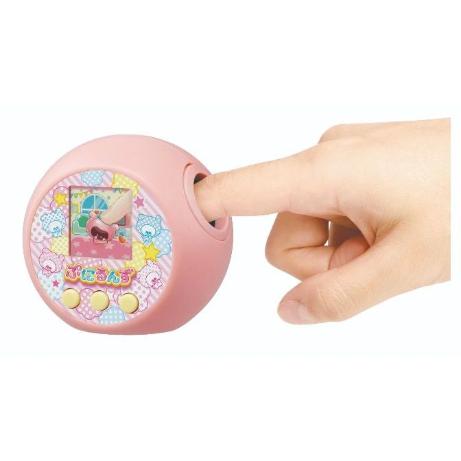  Pink Tamagotchi with finger pressing the squishy top, screen shows a character in a room.