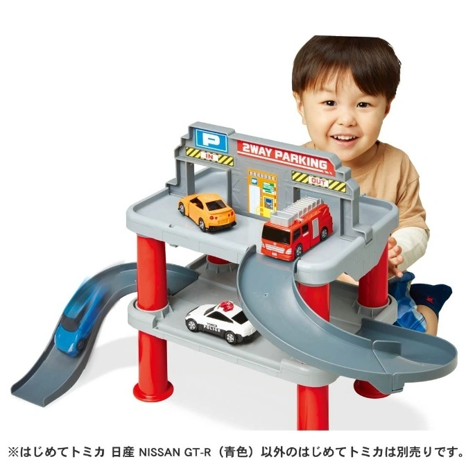  Toy parking garage with toy cars, including a police car, fire truck, and sports car. A child is smiling behind it.