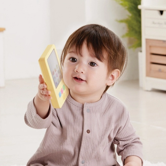  Baby holding a yellow toy phone with colorful buttons and a screen.