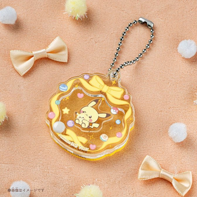  Pikachu charm with yellow bow, beads, and ball chain on peach fabric with bows and pom poms.