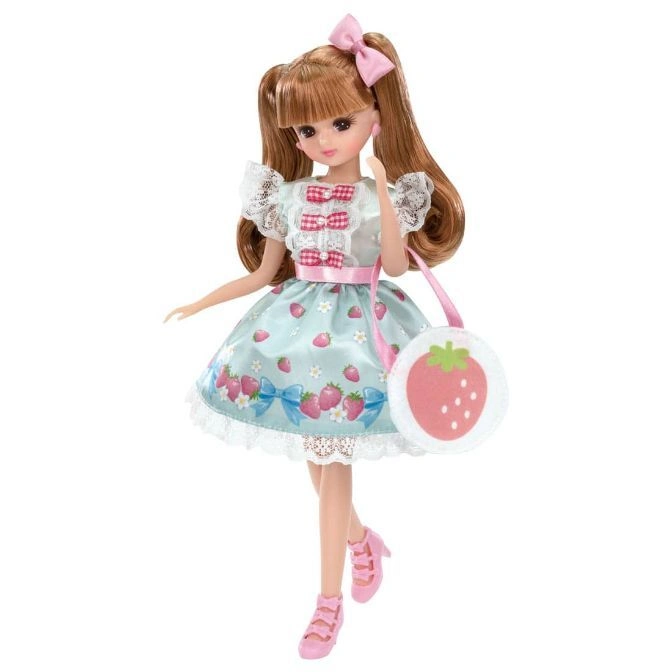 Doll with strawberry dress, bag, and pink bow.  She wears pink shoes and has brown hair in pigtails.
