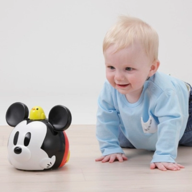  Baby crawling towards a Mickey Mouse toy with a yellow bird on top.