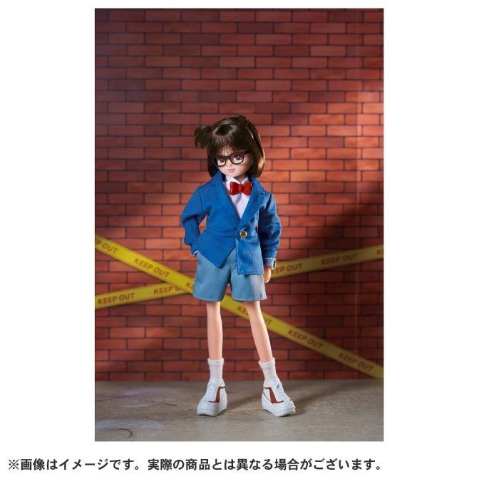 Conan Edogawa doll in blue suit, red bow tie, shorts, sneakers, standing in front of brick wall with caution tape.