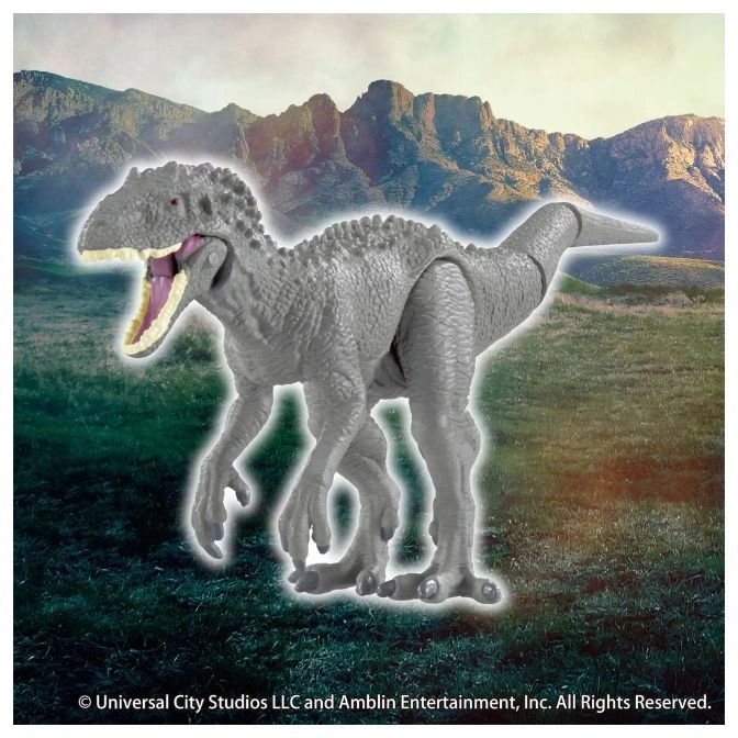  Grey Indominus Rex toy with an open mouth standing on a grassy field with mountains in the background.