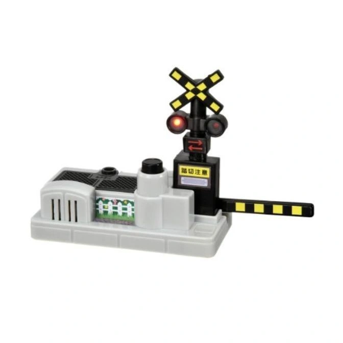 Toy train crossing signal with flashing red lights, striped barrier, and decorative fence scene.