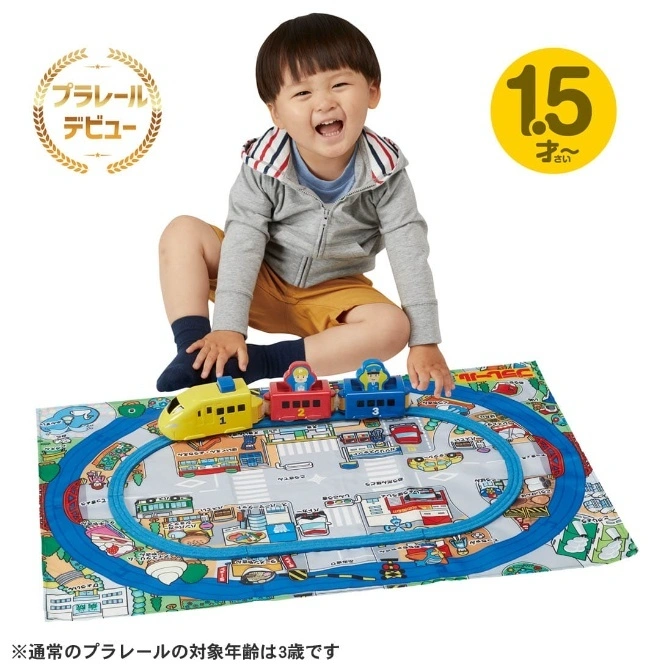  Child playing with a toy train set on a playmat with roads and buildings. The train is yellow, red, and blue.