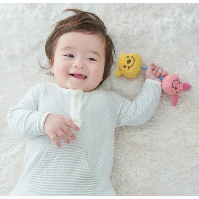  Baby lying on a fluffy rug, smiling and holding a Winnie the Pooh and Piglet rattle.