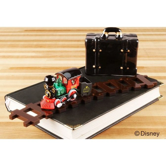  Toy train on a track atop a book, with a black suitcase behind it.