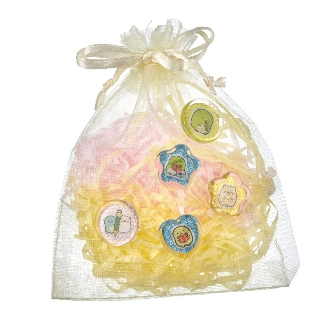  Sumikko Gurashi character badges in a sheer gift bag with yellow and pink crinkle paper.