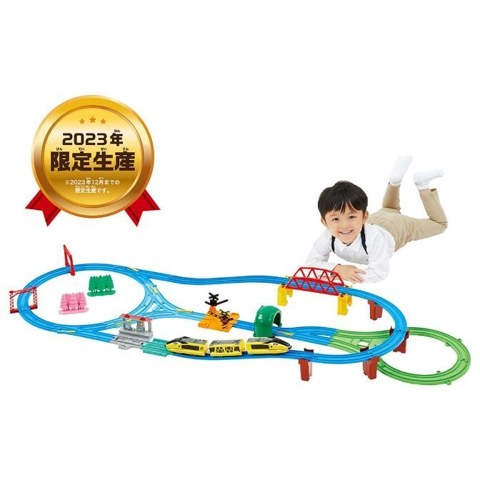 Toy train set with a child lying next to it, featuring a yellow train and blue tracks.