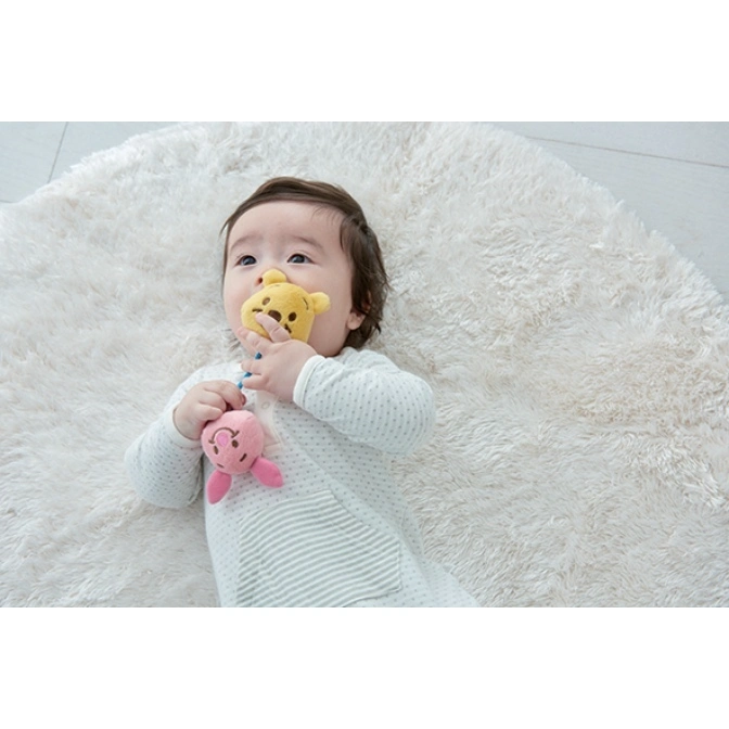  Baby lying on rug with plush bear and piglet toys attached to a pacifier clip.