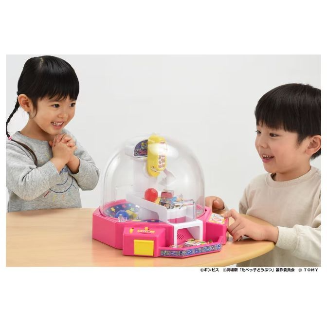  Kids playing with a pink UFO catcher toy with a clear dome and prizes inside.