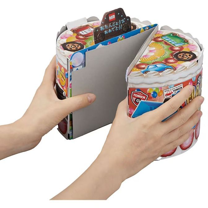  Tomica cake-shaped toy being opened, revealing car-themed decorations and a cardboard car.