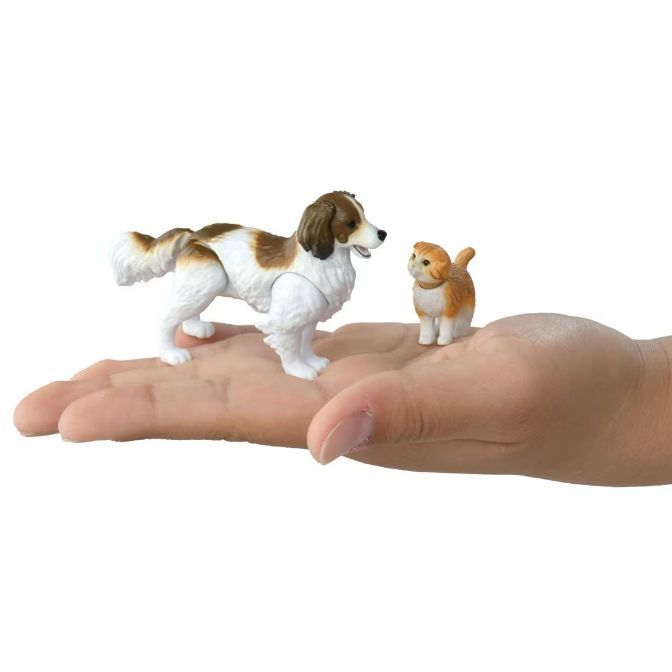  Toy dog and cat figures on a hand. The dog is brown and white, and the cat is orange and white.